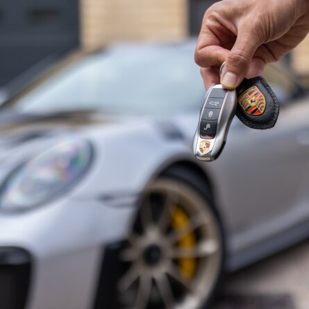 Autoschlüssel mit Porsche im Hintergrund