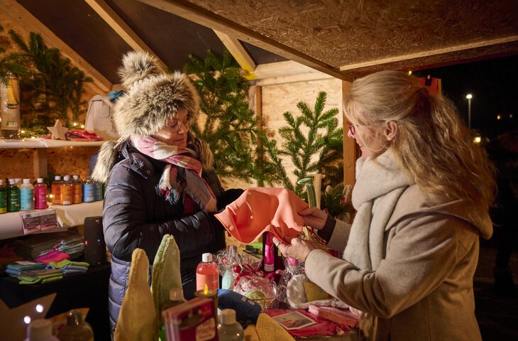 Frau hinter einem Stand auf dem Weihnachtsmarkt berät eine Kundin