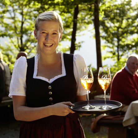 Eine blonde Service-Mitarbeiterin in Tracht hält lächelnd ein Tablett mit zwei Getränken 