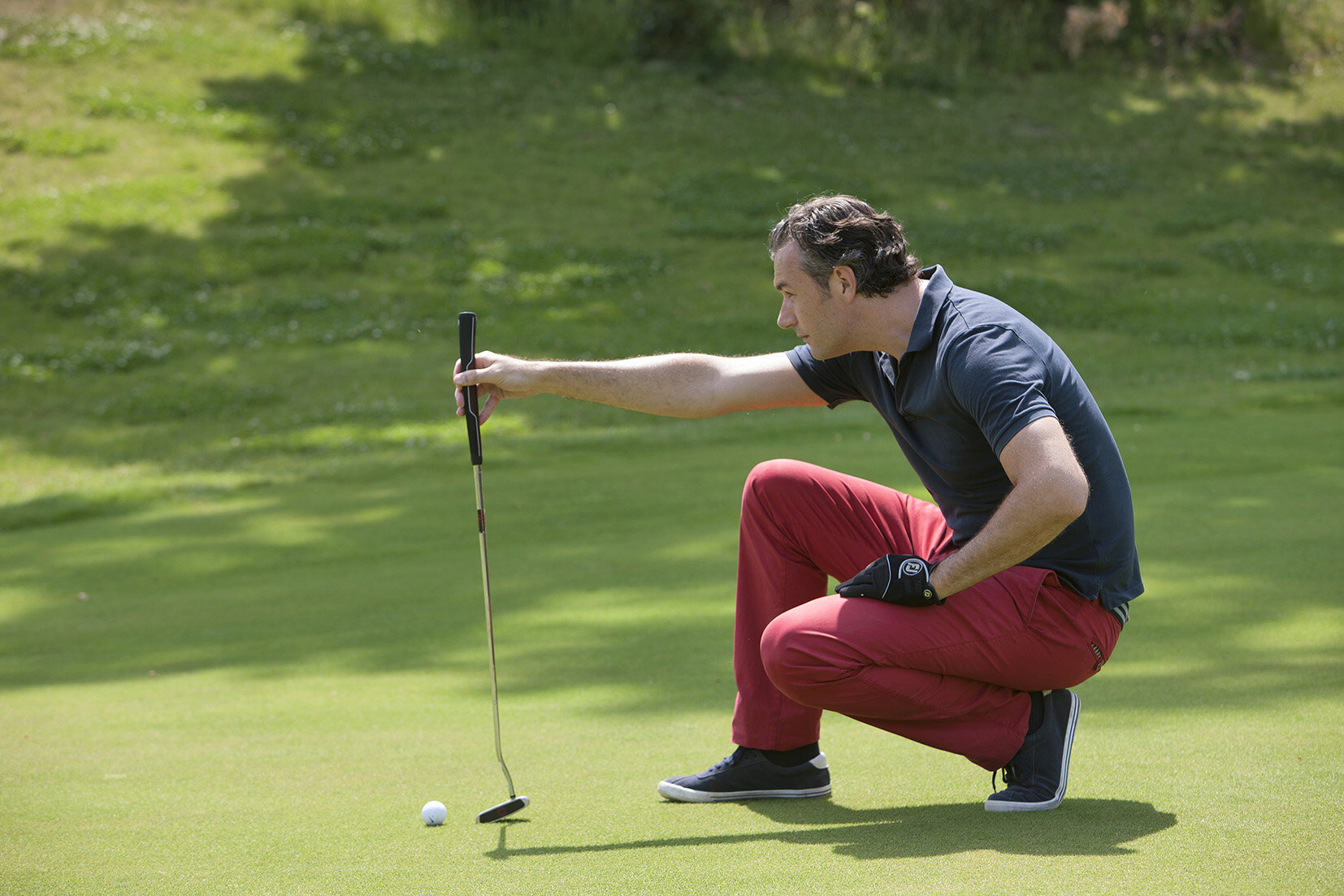 Ein Golfer in roter Golf Hose kniet auf dem Platz und analysiert genau seinen nächsten Abschlag