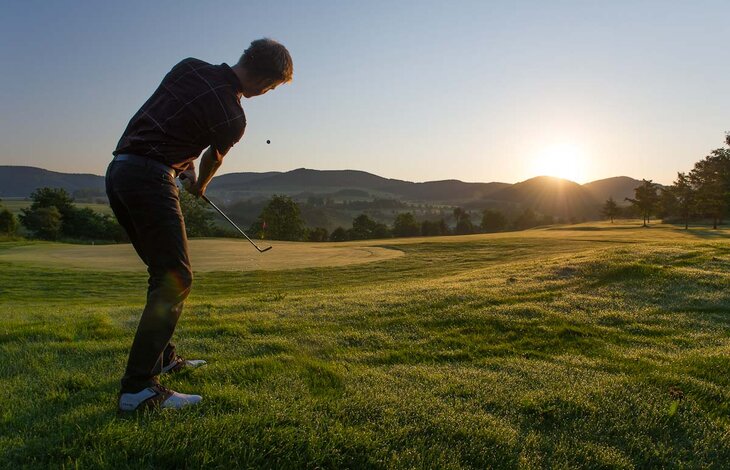 Ein Mann spielt Golf bei Sonnenuntergang im Golfhotel in NRW