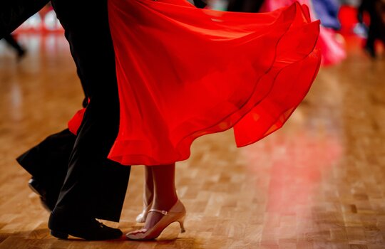 Eine Frau im roten Kleid und eine Mann im Anzug tanzen gemeinsam