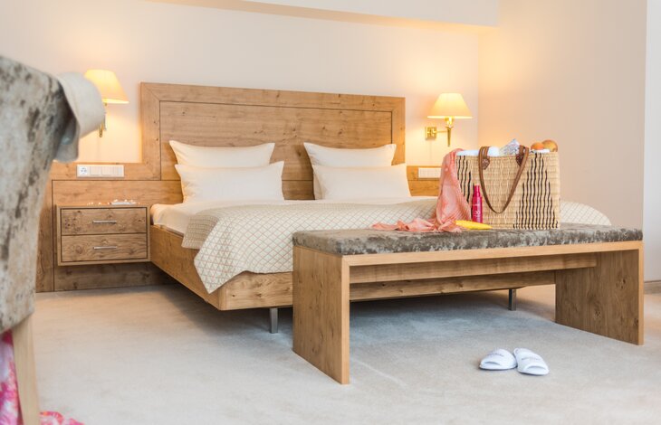 Das Doppelbett des Doppelzimmers Haupthaus im Romantik- und Wellnesshotel Deimann mit moderner Holzoptik und einer großen Wellnesstasche darauf 