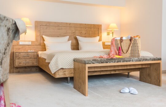 Das Doppelbett des Doppelzimmers Haupthaus im Romantik- und Wellnesshotel Deimann mit moderner Holzoptik und einer großen Wellnesstasche darauf 