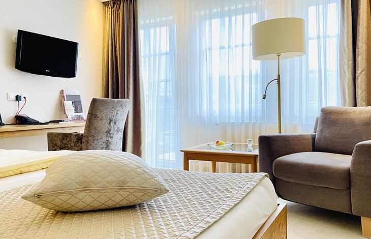 Das Doppelzimmer Haupthaus Knollenblick im Romantik- und Wellnesshotel Deimann mit einem großen grauen Sessel, Schreibtisch und großen Fenstern 