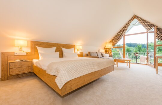 Ein großes Doppelbett aus modernem Holz in einem hellen Dachgeschosszimmer