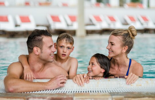 Eine vierköpfige Familie am Beckenrand eines Swimming Pools in ihrem Familienurlaub Sauerland