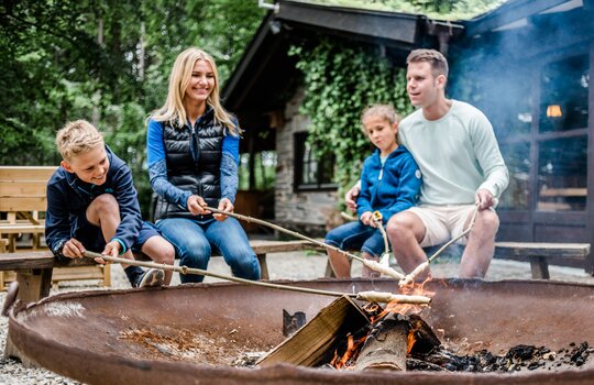 Eine vierköpfige Familie verbringt ihren Familienurlaub in NRW und sitzt an einer Feuerschale mit Stockbrot und 