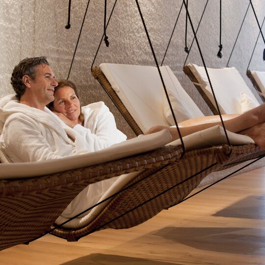 Ein Paar im weißen Bademantel sitzt  während ihres Wellnessurlaubes im Sauerland in einer Hängeliege aneinander gekuschelt