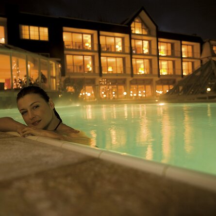 Eine Frau badet bei Nacht im beleuchteten Pool während ihres Wellnessurlaubes im Sauerland 