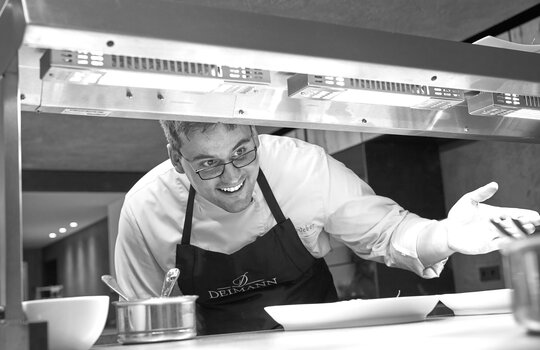 Der Koch, Felix Weber, zeigt lächelnd auf seine Arbeit 