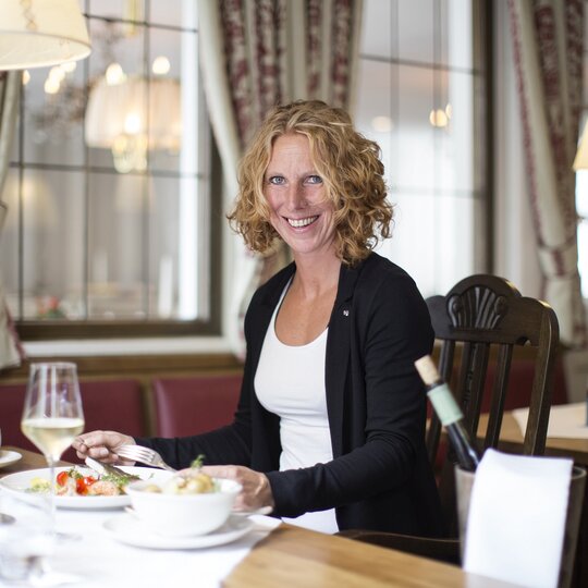 Eine Frau sitzt lächeln vor ihrem Essen im Restaurant Bauernstube im Schwesterhotel Störmann