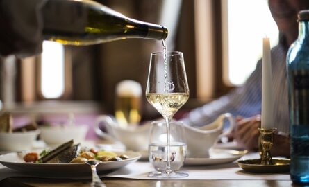 Ein Glas Weißwein wird an einem gedeckten Tisch im Restaurant Bauernstube im Schwesterhotel Störmann eingeschenkt