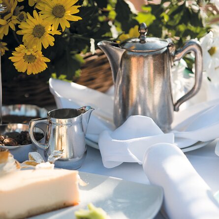 Eine große silberne Kaffeekanne mit einer Milchkanne und einem Käsekuchen auf der Terrasse