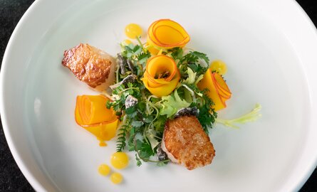 Ein stillvoll angerichtetes Gourmetgericht mit angebratenen Jakobmuscheln, Salat- und Rosengarnitur