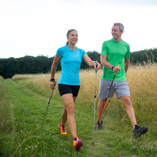 Ein Mann und eine Frau mit ihren Nordic Walking Stöcken beim Wandern durch grüne Wiesen