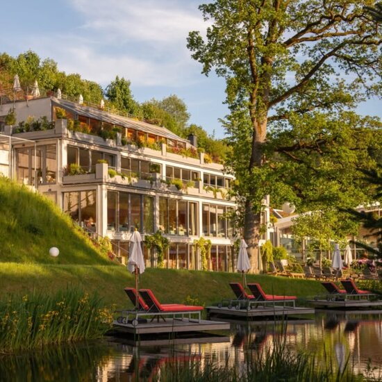 Hotelanlage am Teich mit Grünflächen, Liegestühlen und Sonnenschirmen; mehrstöckige Hotelgebäude im Hintergrund; Schriftzug Green Therapy über dem Teich.