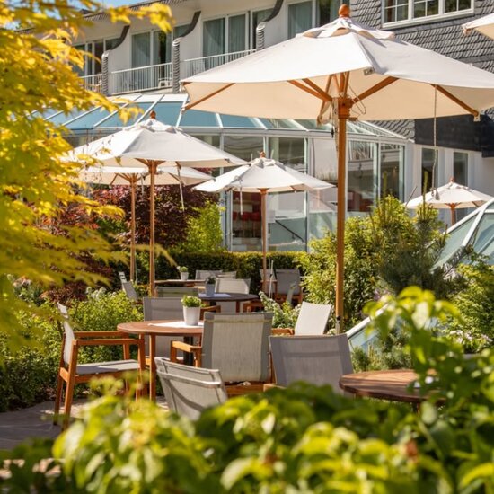 Außenbereich eines Hotelrestaurants mit Holztischen und -bänken, roten karierten Tischdecken, Blumentöpfen und grünem Umfeld.