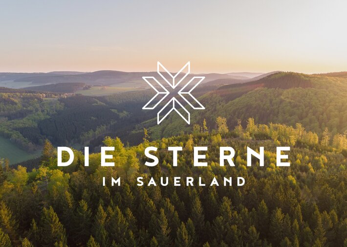 Luftaufnahme einer bewaldeten Hügellandschaft bei Sonnenuntergang mit weißem Stern-Logo und dem Schriftzug DIE STERNE IM SAUERLAND.