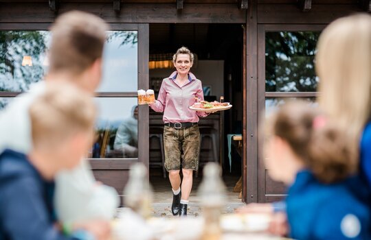 Freundliche Bedienung in der Knollenhütte trägt Speisen nach draußen