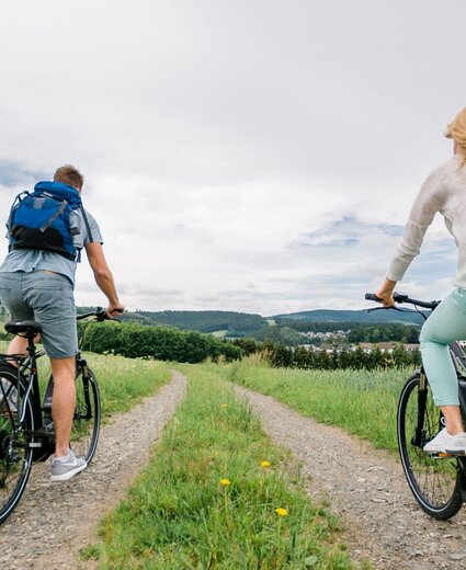 Eine Frau und ein Mann fahren gemeinsam auf Fahrrädern durch die grüne Landschaft des Sauerlands