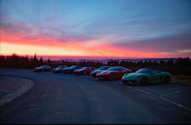 Mehrere Porsche Wagen stehen bei Sonnenuntergang nebeneinander