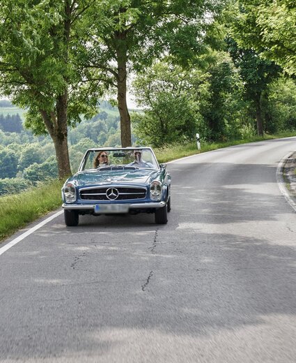 Pärchen fährt mit dem Mercedes Oldtimer über die Straße