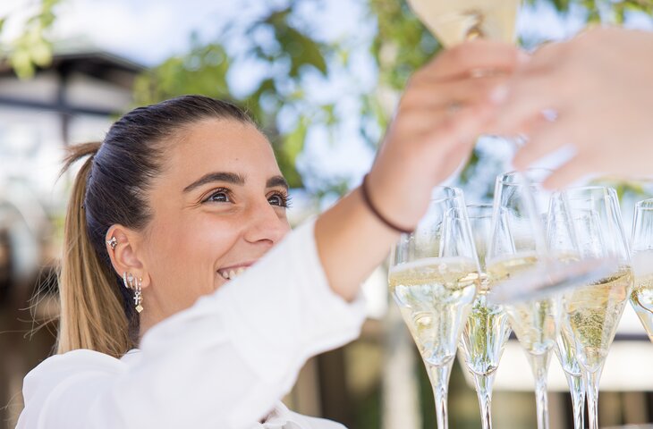 Freundliche Servicekraft reicht einem Gast ein Glas Sekt